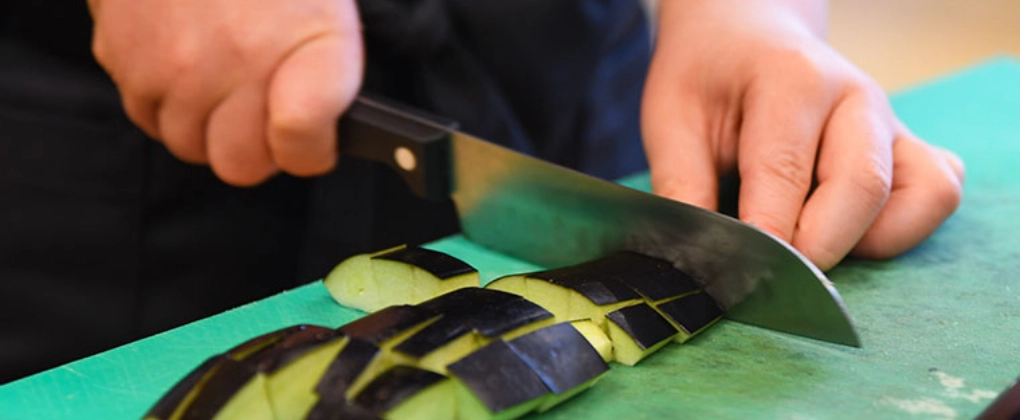 VielfaltMenü cook-at-school Kind schneidet Aubergine