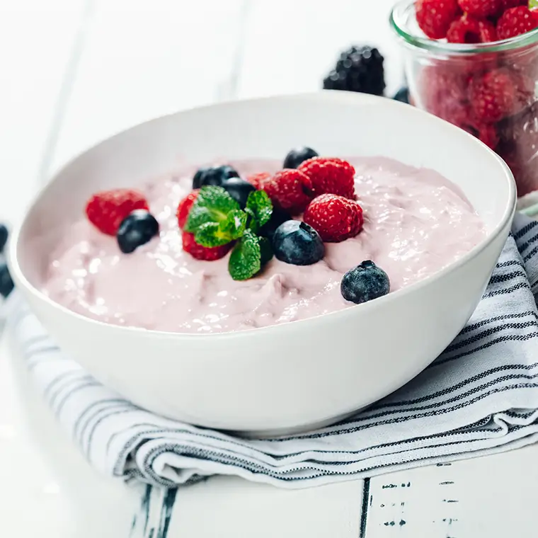 A bowl of creamy fruit quark garnished with fresh raspberries, blueberries and mint leaves.