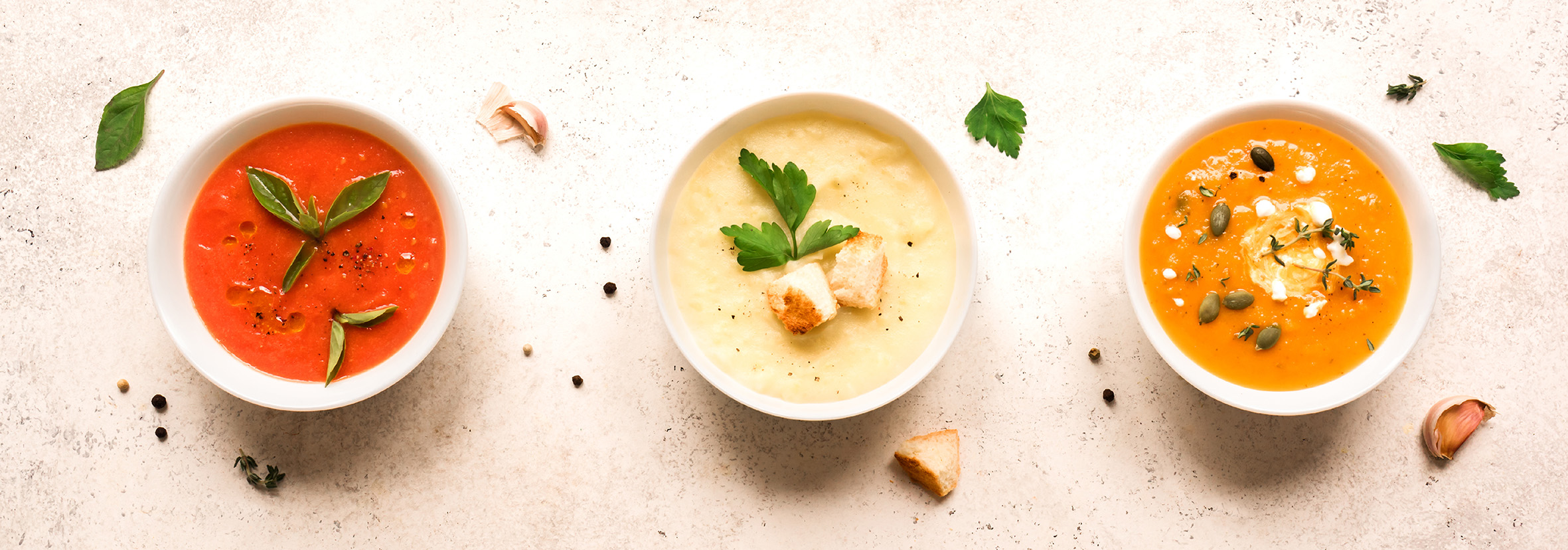 Drei verschiedene pürierte Gemüsesuppen in weißen Schalen, angerichtet mit Kräutern und Kernen.